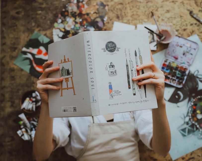 An artist reads an art book surrounded by painting supplies, embracing creativity and relaxation.