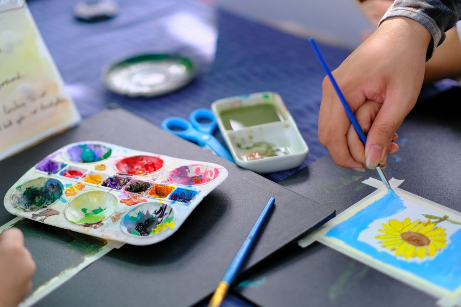 Close-up of hands using watercolors to paint a sunflower. Capturing artistic expression and creativity.
